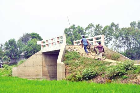 Due to lack of earth on the connecting road, people are crossing a bridge on Mamudnagar Post Kamari road in Nagarpur Upazila of Tangail with difficulty. 	photo: Observer 