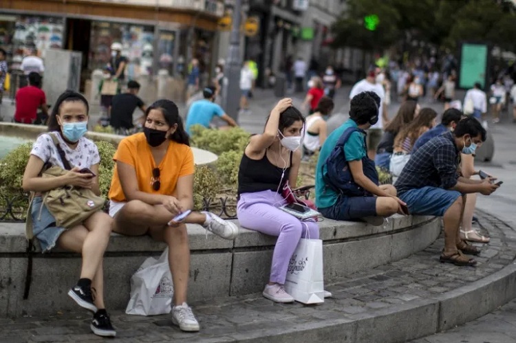 People wearing face masks to prevent the spread of coronavirus sit on stone benches in downtown Madrid, Spain, Tuesday, July 28, 2020. The Madrid regional government is making the use of face masks mandatory in all public areas, limiting how many people can gather in one place and targeting young people in a drive to stamp out new outbreaks of COVID-19 (AP Photo)