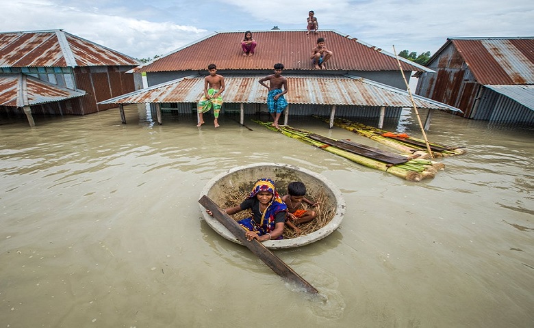 Some of flood-hit people, including children, took shelter in the top of their tin-shed while a mother trying to transport her child to a shelter house during the recent August flood. Photo: BSS